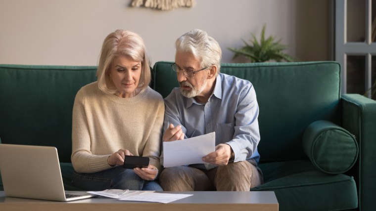 an older couple seated on a couch reading a report