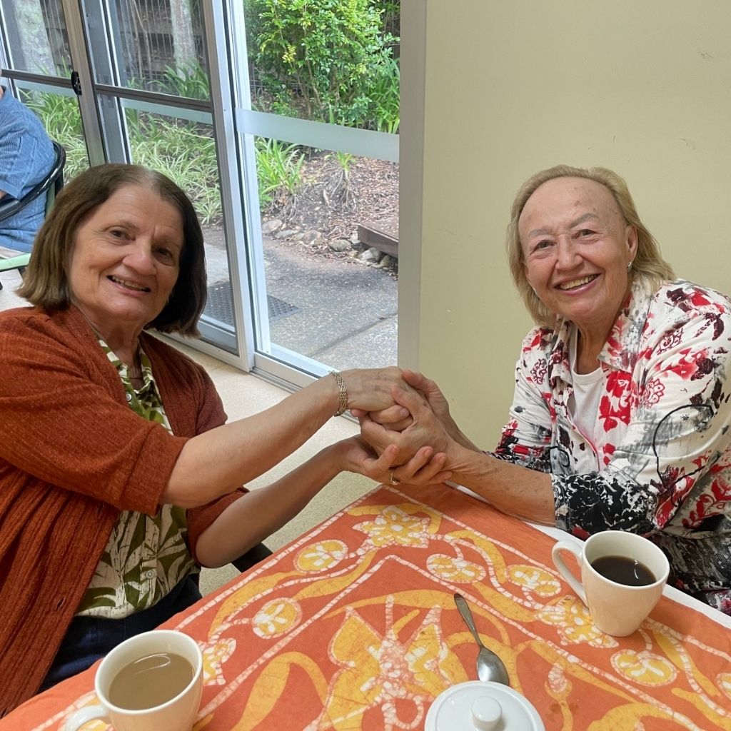two clients smiling and holding hands with a cuppa at our Activity Centre